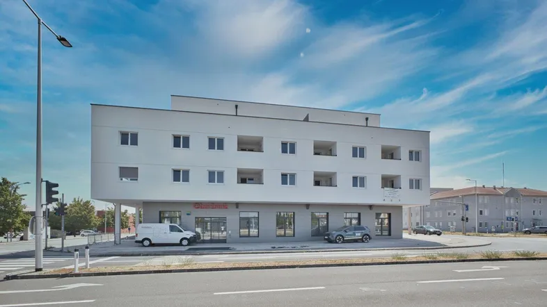 Modernes Gebäude mit Geschäften im Erdgeschoss und Wohnungen darüber an einer Straßenecke.