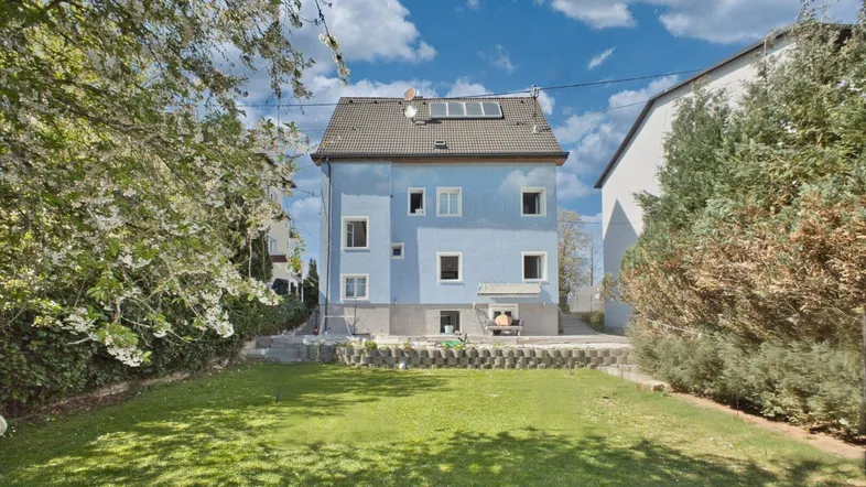 Blaues Einfamilienhaus mit großem Garten und Solaranlage auf dem Dach.