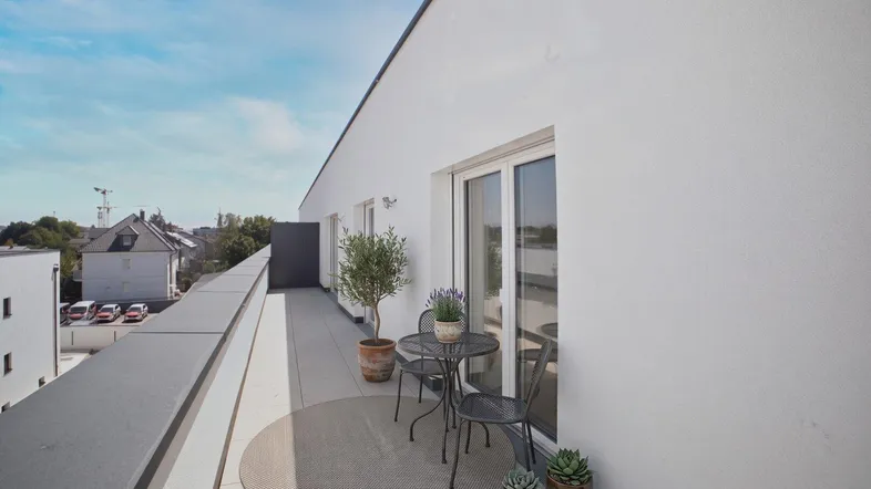 Möblierter Balkon mit Sitzgelegenheiten und Blick auf die Umgebung unter blauem Himmel.