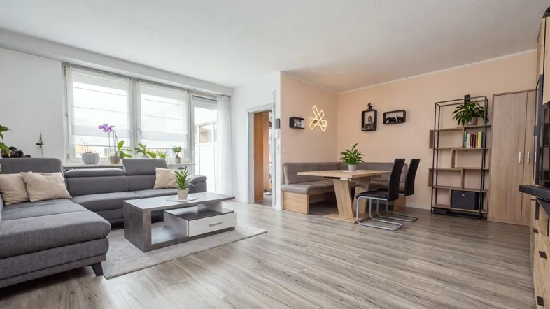 Heller offener Wohn- und Essbereich mit modernem Laminatboden und Zugang zum Balkon.