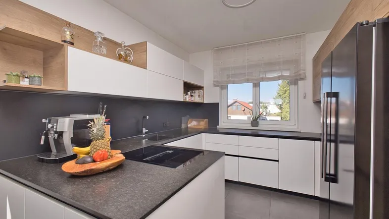 Moderne Küche mit weißen Hochglanzfronten, dunkler Arbeitsplatte und Fenster mit Blick ins Grüne.