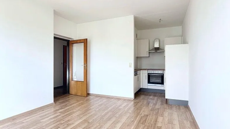 Helles, leeres Zimmer mit Laminatboden und offenem Zugang zu einer Küchenzeile.