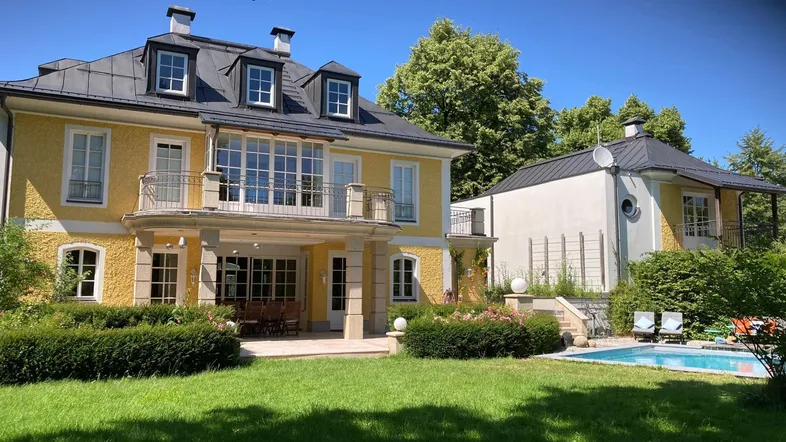 Gelbe Villa mit großem Garten, Pool und separatem Nebengebäude unter blauem Himmel.