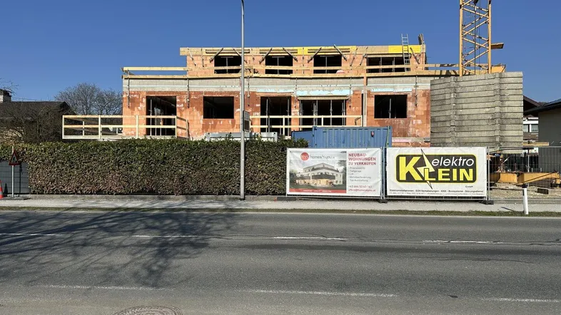 Baustelle eines Neubaus mit sichtbaren Ziegelwänden und Baugerüst unter blauem Himmel.