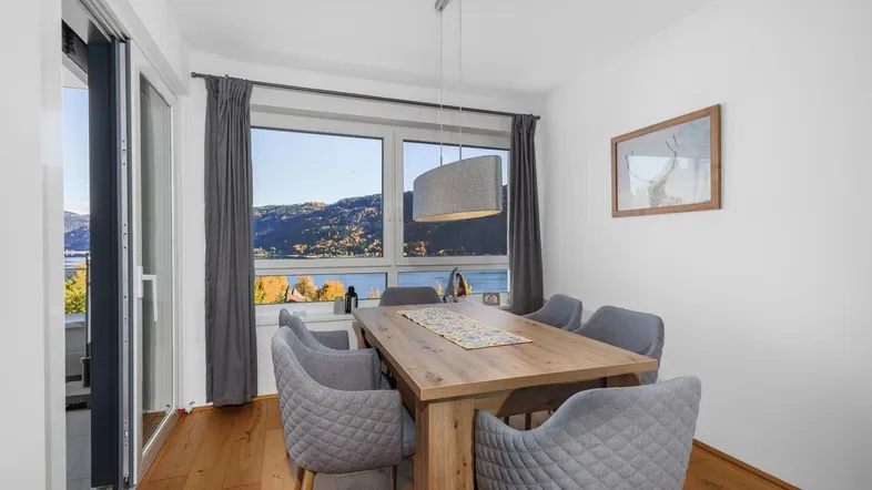 Heller Essbereich mit Holztisch, modernen Stühlen und direktem Zugang zum Balkon mit Seeblick.