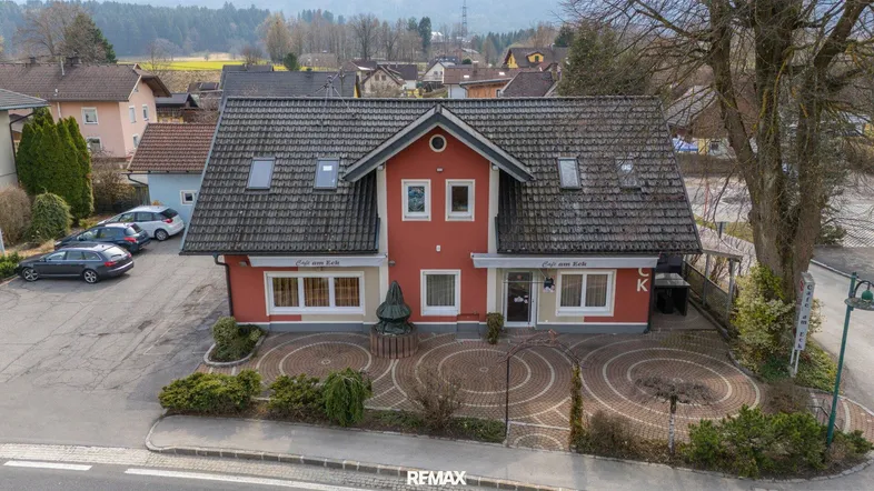 Gebäudeansicht von oben mit roter Fassade, Schrägdach und gepflastertem Vorplatz.
