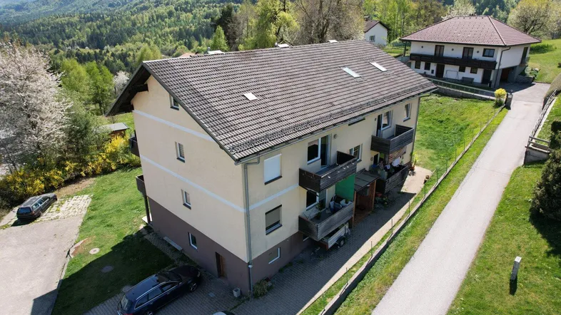 Luftaufnahme eines Mehrfamilienhauses mit Balkonen und Bergblick in grüner Umgebung.