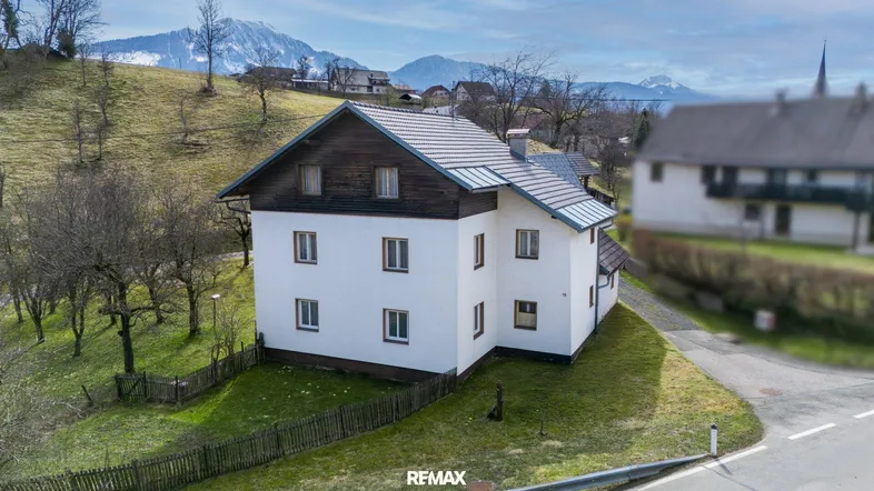 Freistehendes Haus mit weißer Fassade und dunklem Dach in ländlicher Umgebung mit Bergblick.