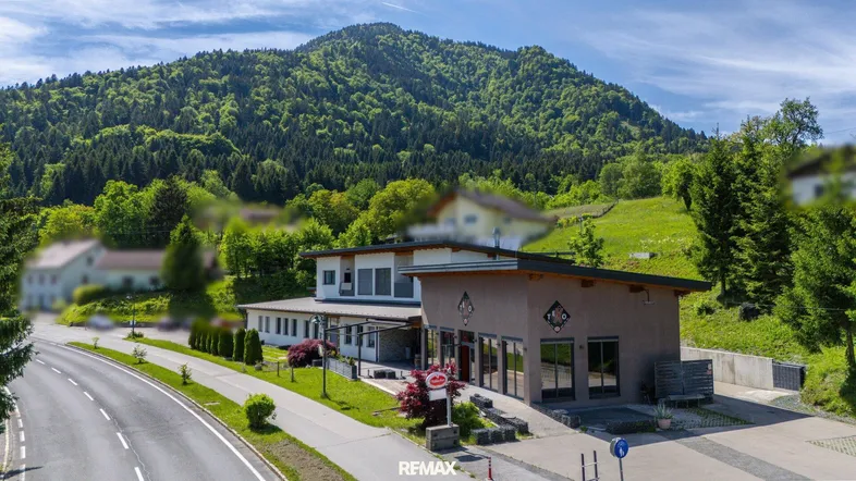 Gebäudeensemble mit moderner Architektur und umliegender Natur vor einer bewaldeten Bergkulisse.