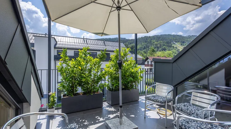 Sonnenterrasse mit Sitzgelegenheiten, Pflanzen und weitem Blick auf die Berge.