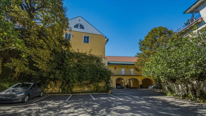 Außenansicht eines gelben Gebäudes mit Parkplätzen und viel Grünfläche unter blauem Himmel.