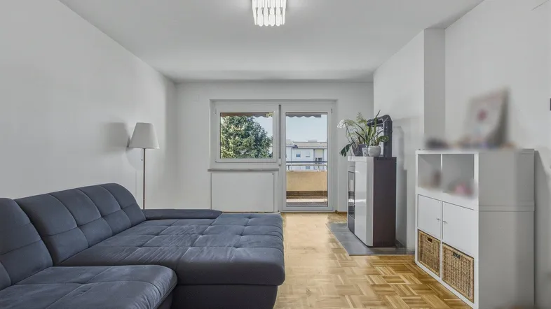 Helles Wohnzimmer mit Parkettboden, großem Sofa und Zugang zum Balkon.