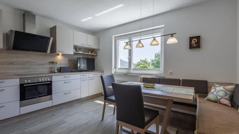 Moderne Wohnküche mit Essbereich, hellen Schränken, Holzakzenten und Fenster mit Ausblick ins Grüne.