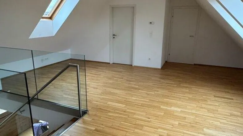 Offener Wohnbereich im Dachgeschoss mit Parkettboden, Glasgeländer und Dachfenstern.
