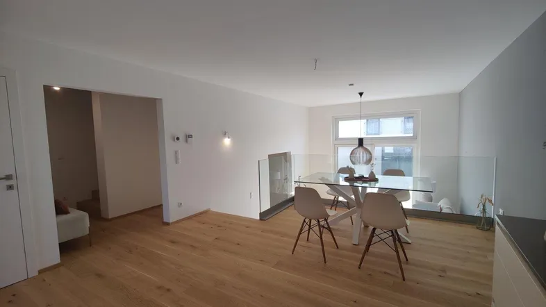Offener Wohn- und Essbereich mit Glasgeländer, Holzboden und großen Fenstern für viel Licht.