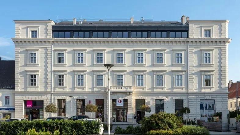 Klassische Fassade eines Altbaus mit modernem Dachausbau und großen Fenstern in städtischer Umgebung.