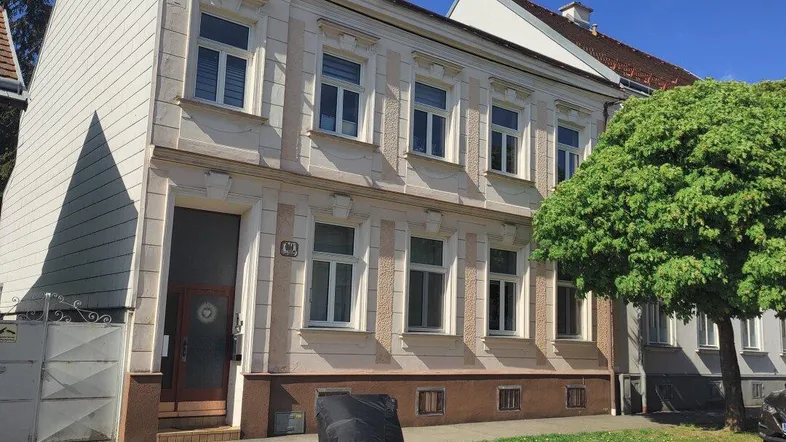 Historisches Mehrfamilienhaus mit klassischer Fassade und einem großen Baum davor an einem sonnigen Tag.