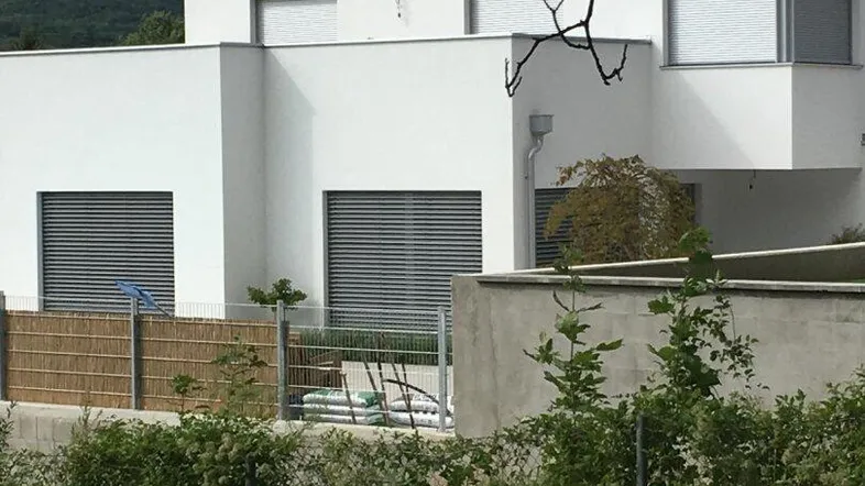 Moderne weiße Fassade eines Gebäudes mit großen Fenstern und Rollläden.