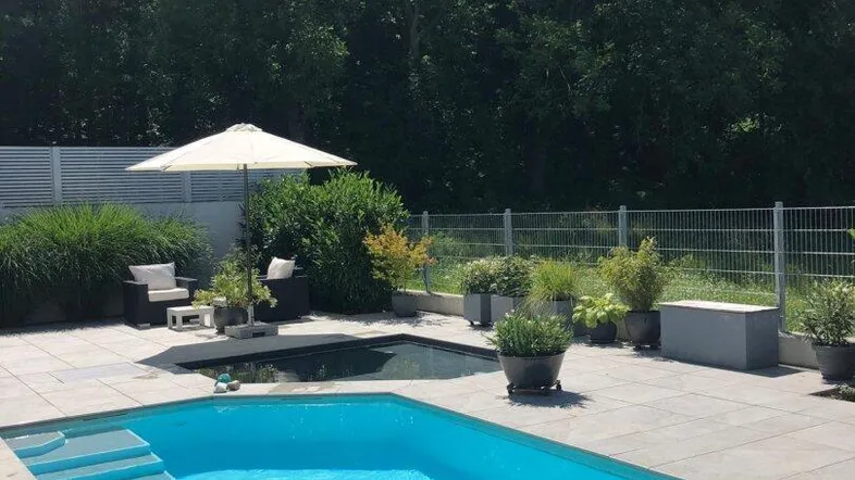 Großer Außenbereich mit modernem Pool, Liegefläche und üppiger Bepflanzung im Hintergrund.