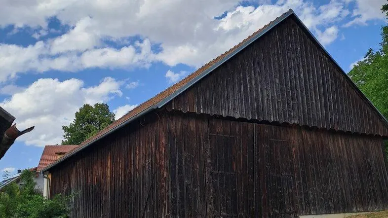 Langes Holzgebäude mit Satteldach und dunkler Holzfassade unter bewölktem Himmel.