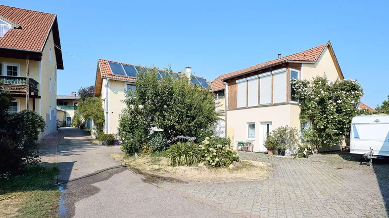 Mehrere Gebäude mit gepflasterter Zufahrt und begrünten Bereichen unter blauem Himmel.