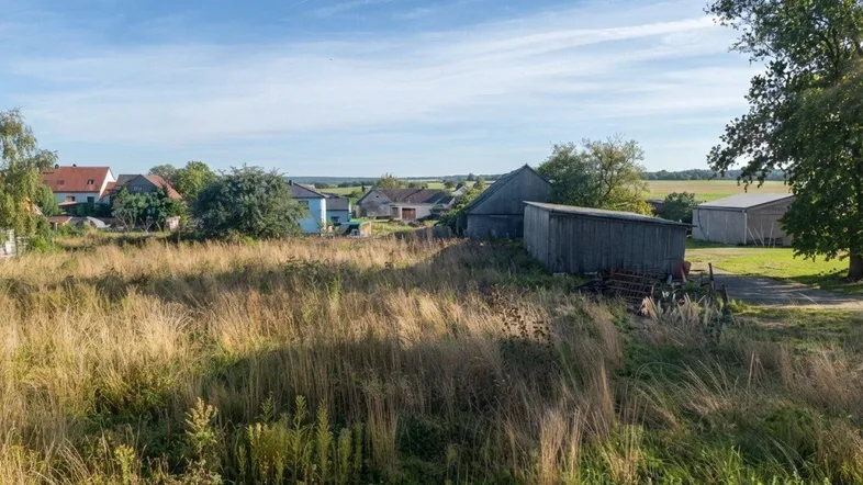 Weitläufige ländliche Landschaft mit Feldern, Bauernhöfen und Wohnhäusern unter blauem Himmel.