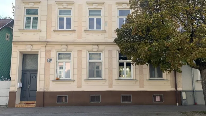 Vorderansicht eines klassischen Mehrfamilienhauses mit beiger Fassade und braunem Sockel.