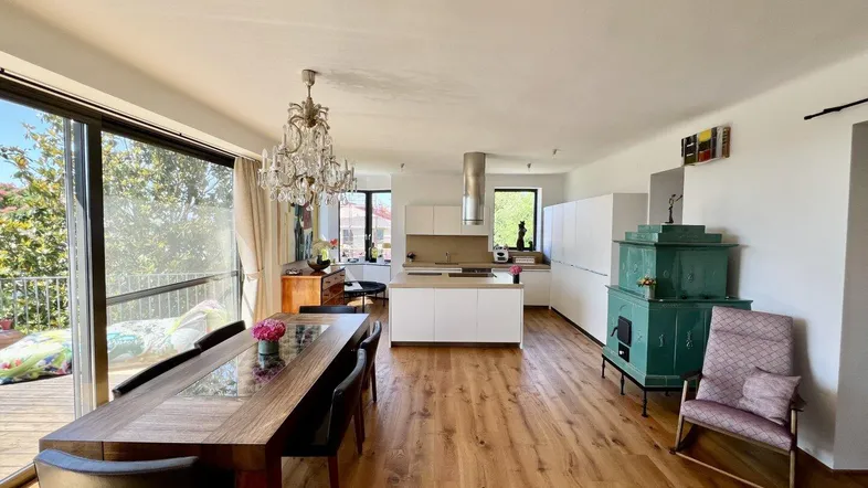 Geräumiger offener Wohn-Essbereich mit moderner Küche, Holzboden und Zugang zum Balkon.