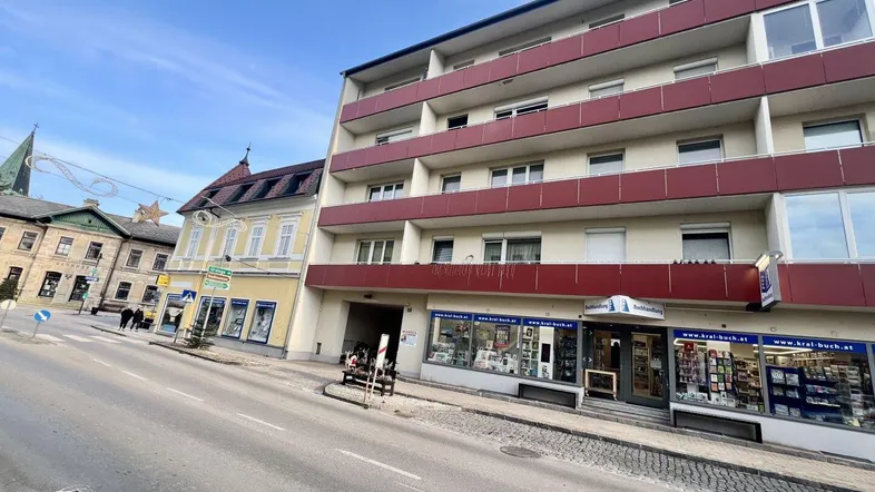 Mehrstöckiges Gebäude mit Geschäften im Erdgeschoss und Balkonen an der Fassade, an einer Straße gelegen.