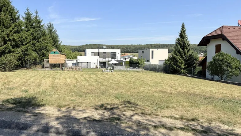 Weitläufiges Grundstück mit Blick auf moderne Häuser und grüne Umgebung unter blauem Himmel.
