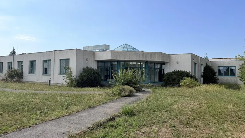 Gebäude mit moderner Architektur, großen Fenstern und einer Glaskuppel, umgeben von Rasenflächen.