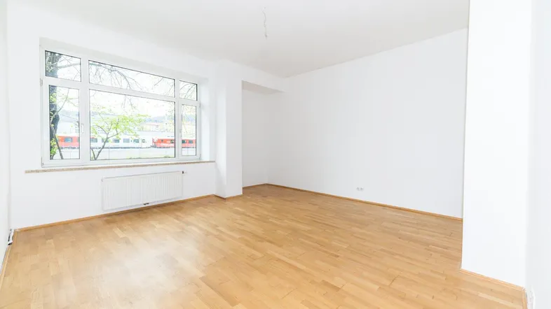 Helles, leeres Zimmer mit Parkettboden und großem Fenster, bereit zur individuellen Gestaltung.