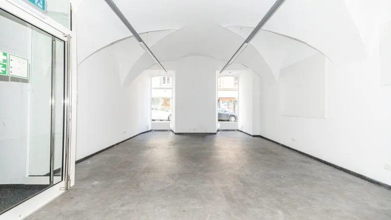 Geräumiger, leerer Raum mit Gewölbedecken, Betonboden und großen Fenstern zur Straße.