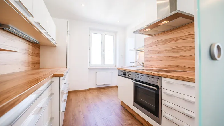 Moderne Küche mit weißen Schränken, Holzarbeitsplatten und integrierten Geräten, hell durch Fenster.