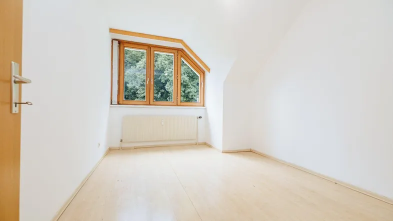 Helles Zimmer mit Dachschräge, Laminatboden und Fenster mit Blick ins Grüne.