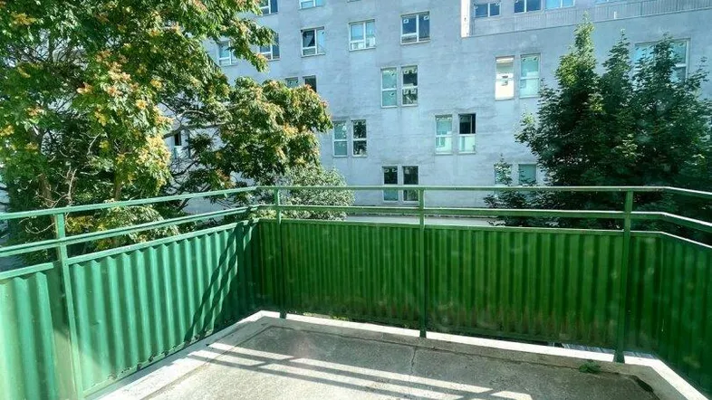 Betonierte Terrasse mit grüner Brüstung und Blick auf das umliegende Gebäude und Bäume.