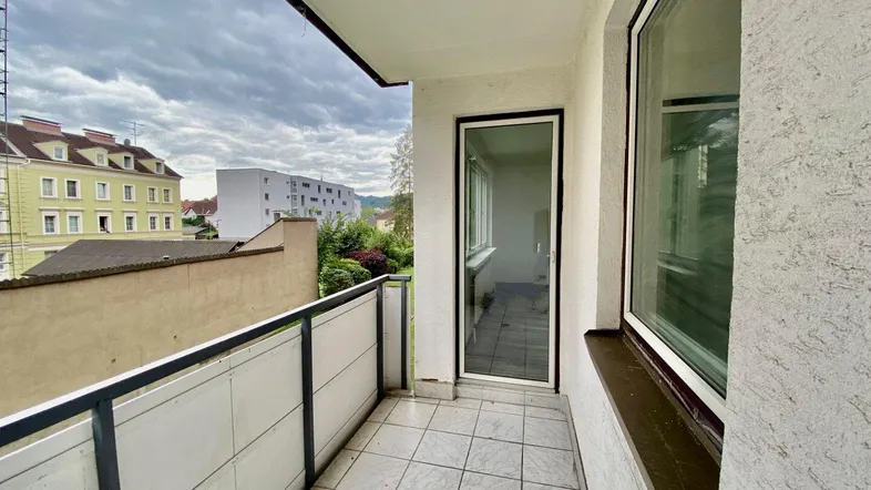 Heller Balkon mit Fliesenboden und Blick auf die umliegenden Gebäude unter bewölktem Himmel.