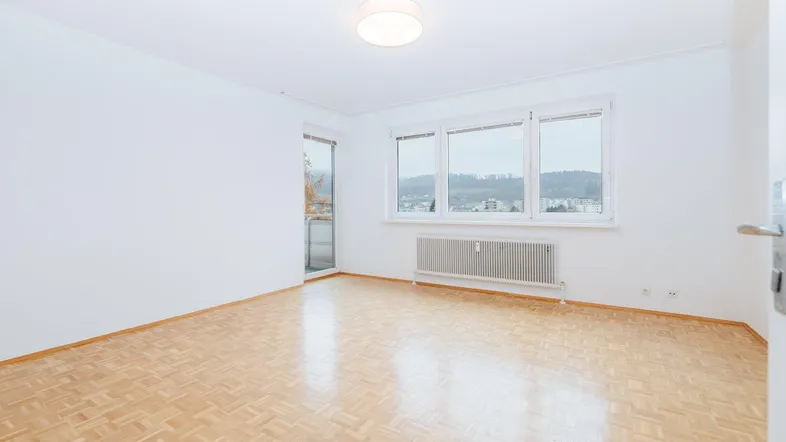 Helles Zimmer mit Parkettboden und Zugang zu einem kleinen Balkon, bietet einen weiten Blick.