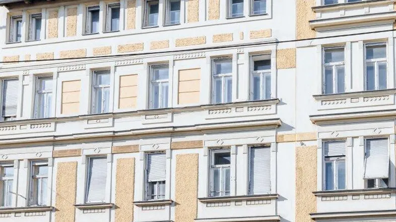Fassade eines Altbaus mit gelb-weißer Farbgebung und vielen Fenstern unter blauem Himmel.