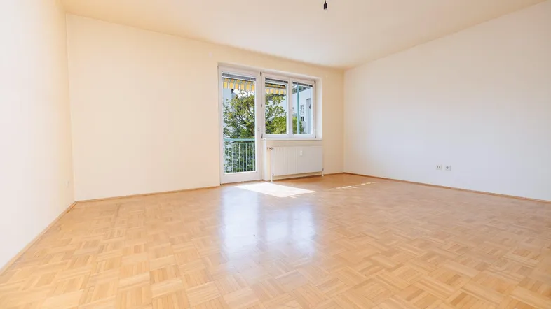 Helles, leeres Zimmer mit Parkettboden und Zugang zu einem Balkon, ideal für Wohn- oder Schlafbereich.