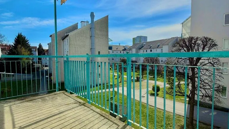 Sonniger Balkon mit Markise und Blick auf die grüne Wohnanlage und den Innenhof.
