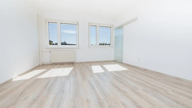 Heller, leerer Raum mit großen Fenstern und modernem Laminatboden, ideal als Wohn- oder Schlafzimmer.