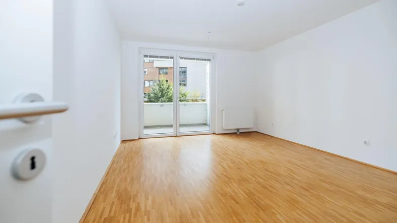 Helles Zimmer mit Parkettboden und Zugang zu einem Balkon, ideal als Wohn- oder Schlafbereich.