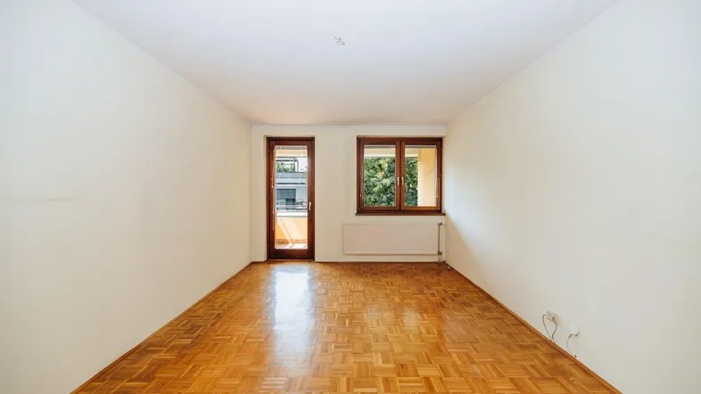Helles Zimmer mit Parkettboden und Zugang zu einem Balkon, ideal als Wohn- oder Schlafzimmer.
