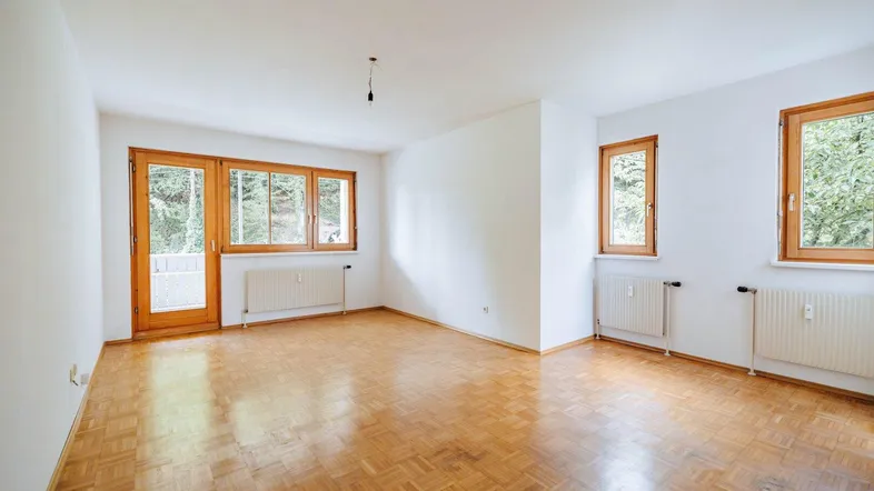 Helles, leeres Zimmer mit Parkettboden, weißen Wänden und Zugang zu einem Außenbereich.
