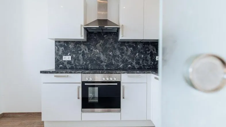 Moderne Küche mit weißen Hochglanzfronten, dunkler Arbeitsplatte und Laminatboden.