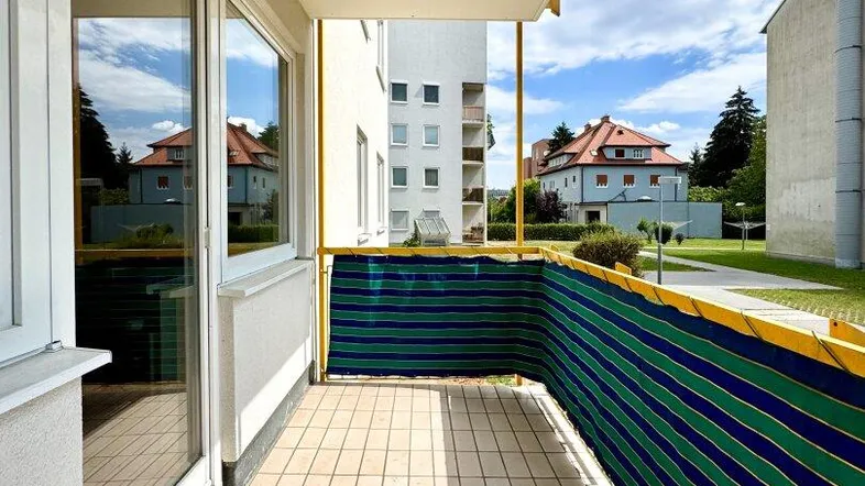 Heller Balkon mit Fliesenboden und Blick auf die umliegenden Gebäude und Bäume.