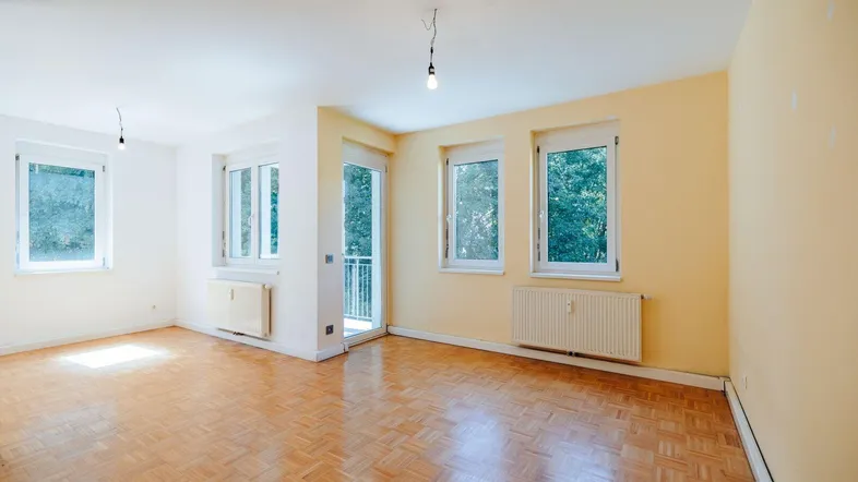 Helles Wohnzimmer mit Parkettboden, gelben Wänden und Zugang zu einem kleinen Balkon.