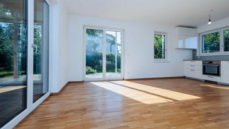 Heller offener Wohnbereich mit Holzboden, großen Glasfronten und Zugang zu einer Terrasse sowie integrierter Küche.