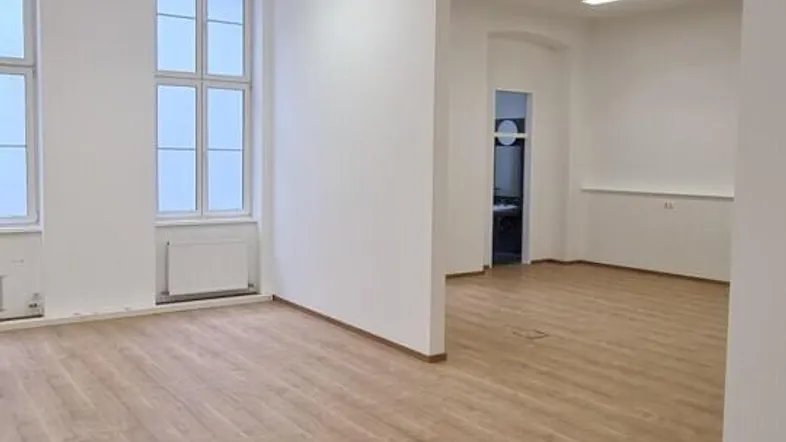Geräumiger, heller Büroraum mit großen Fenstern und modernem Laminatboden.